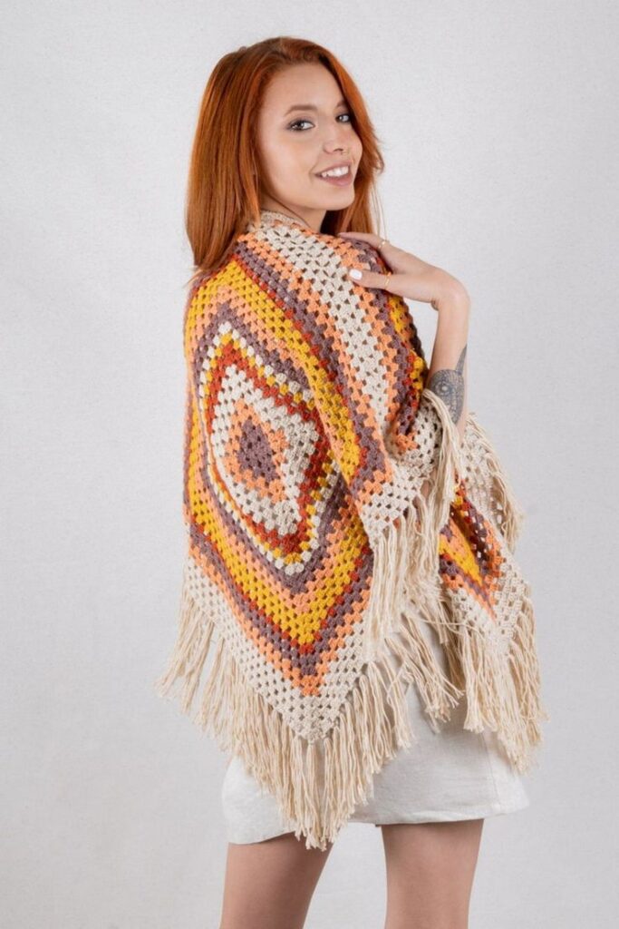 Mulher sorrindo com xale de crochê colorido com franjas em look casual