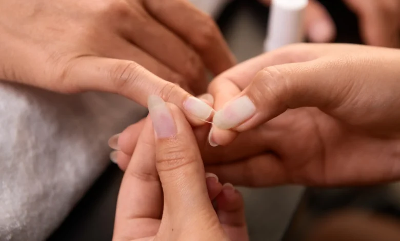 aplicação cuidadosa de unha postiça transparente em dedo feminino.