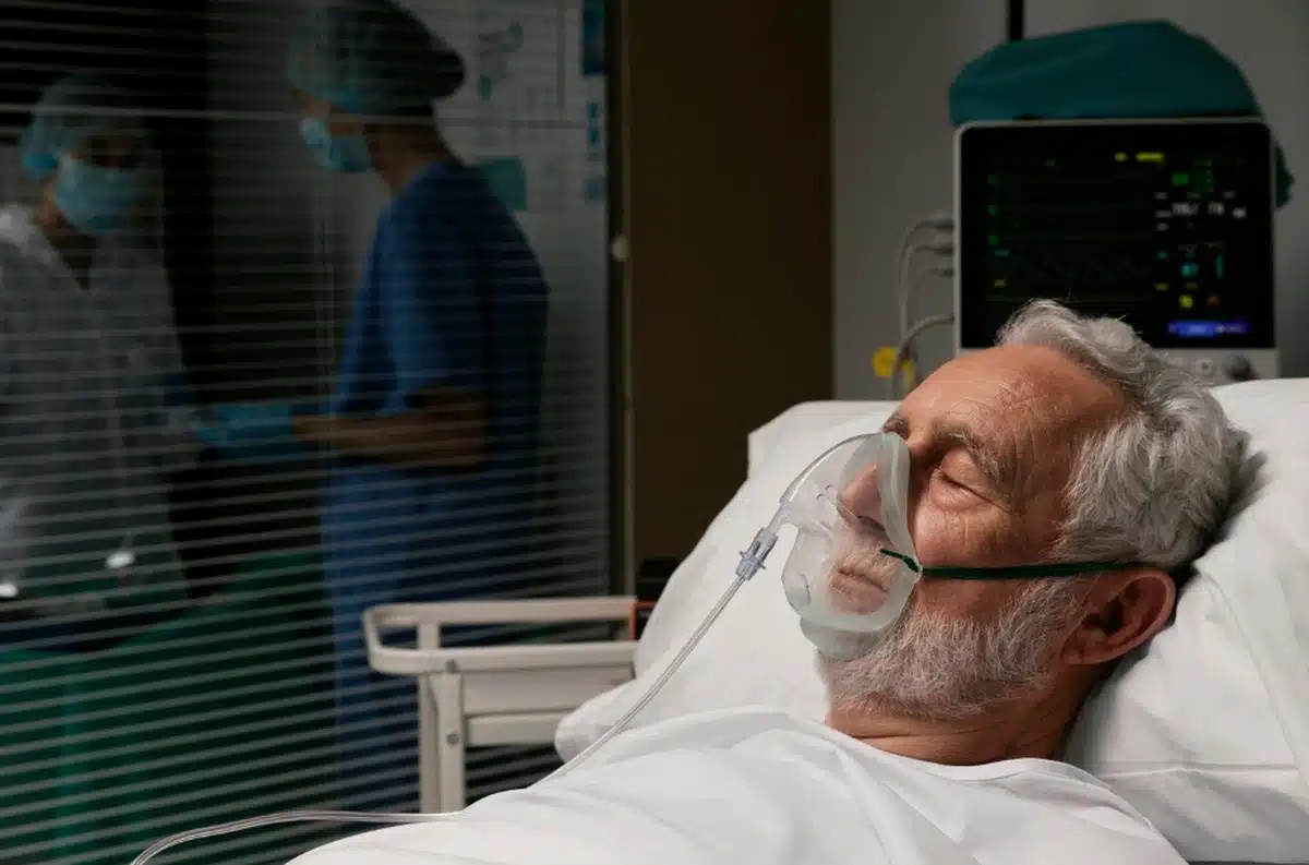 Paciente idoso em hospital recebendo oxigênio por máscara, representando o aumento dos casos de síndrome respiratória aguda grave no país.