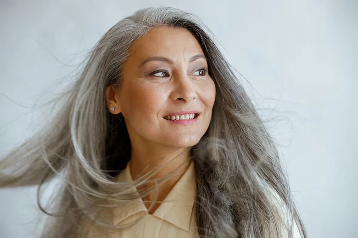 Mulher com cabelos longos e grisalhos sorrindo com confiança, celebrando a beleza sem idade.
