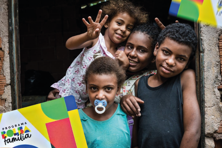 Grupo de crianças posando em frente a uma casa, com cartazes do programa Bolsa Família.