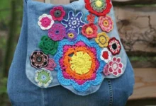 Bolsa jeans decorada com aplicações de flores de crochê coloridas.