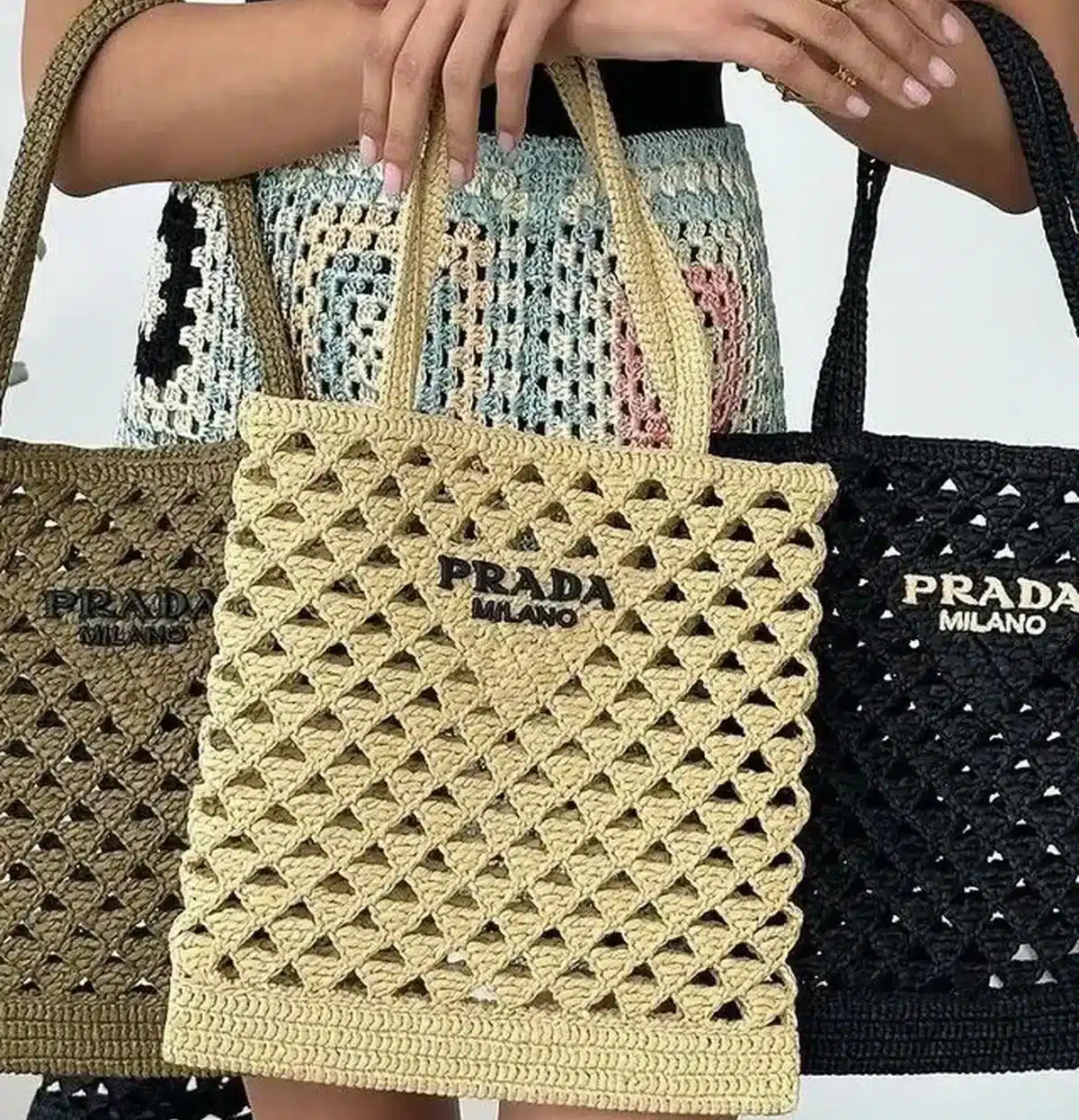 Bolsa de crochê Prada Milano em forma de triângulos, destacando-se nas cores preta, bege e verde.