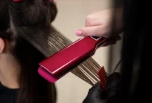 Hairstylist usando uma prancha rosa para alisar cabelo grosso e ondulado durante o tratamento.