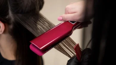 Hairstylist usando uma prancha rosa para alisar cabelo grosso e ondulado durante o tratamento.