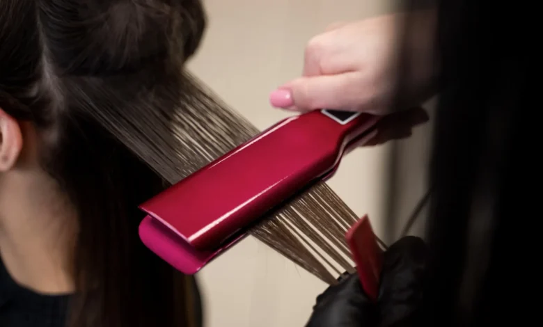 Hairstylist usando uma prancha rosa para alisar cabelo grosso e ondulado durante o tratamento.