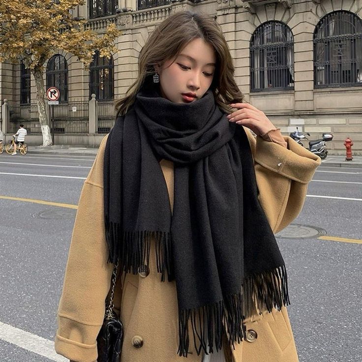 Mulher usando um casaco amarelo e cachecol preto, em uma rua durante o inverno.