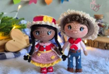 Casal de bonecos amigurumi em estilo junino com roupas típicas e decoração festiva ao fundo