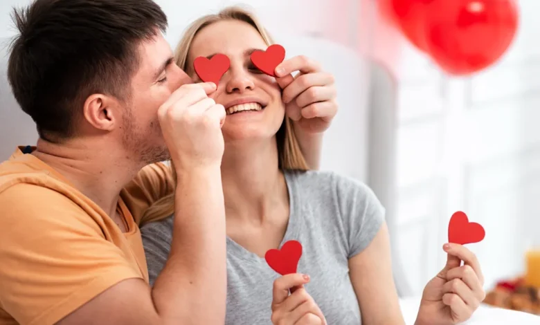 Casal feliz brincando com corações vermelhos para comemorar o Dia dos Namorados em casa