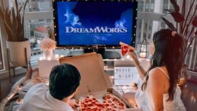 Casal assistindo a um filme em casa, com pizza e ambiente acolhedor.