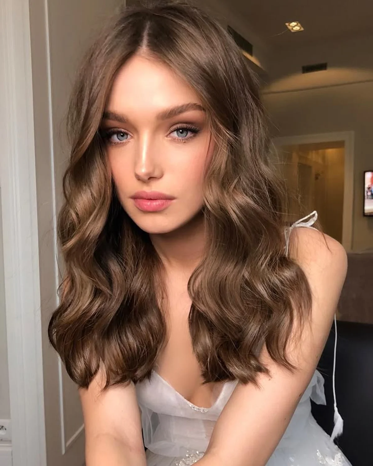 Mulher com cabelo castanho claro ondulado, em corte médio com acabamento natural.