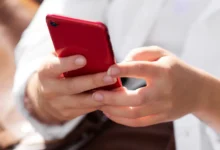 Mulher segurando smartphone vermelho em ambiente ao ar livre, em dia ensolarado.