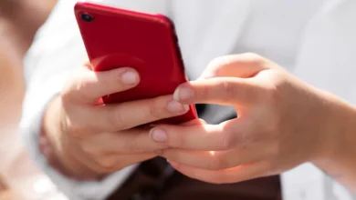 Mulher segurando smartphone vermelho em ambiente ao ar livre, em dia ensolarado.