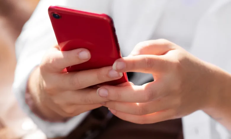 Mulher segurando smartphone vermelho em ambiente ao ar livre, em dia ensolarado.