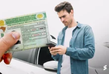 Jovem consulta informações sobre CNH gratuita usando o celular ao lado do carro