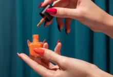 Mão com unhas vermelhas aplicando esmalte laranja, inspiração para o São João