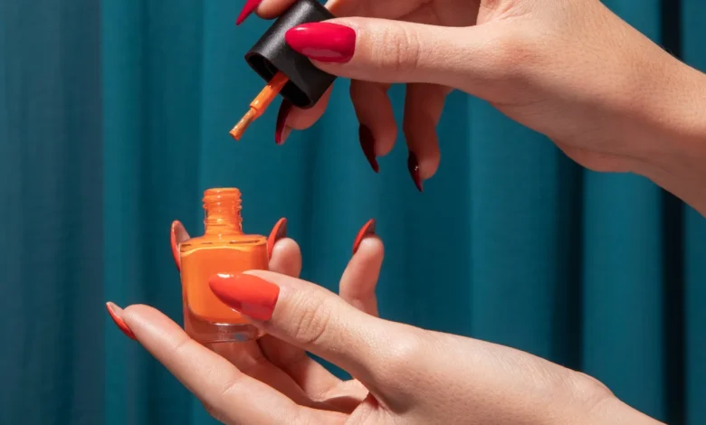 Mão com unhas vermelhas aplicando esmalte laranja, inspiração para o São João