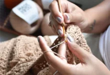 Pessoa fazendo crochê com linha bege e agulha, criando uma peça artesanal.