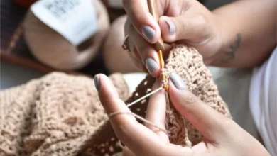 Pessoa fazendo crochê com linha bege e agulha, criando uma peça artesanal.