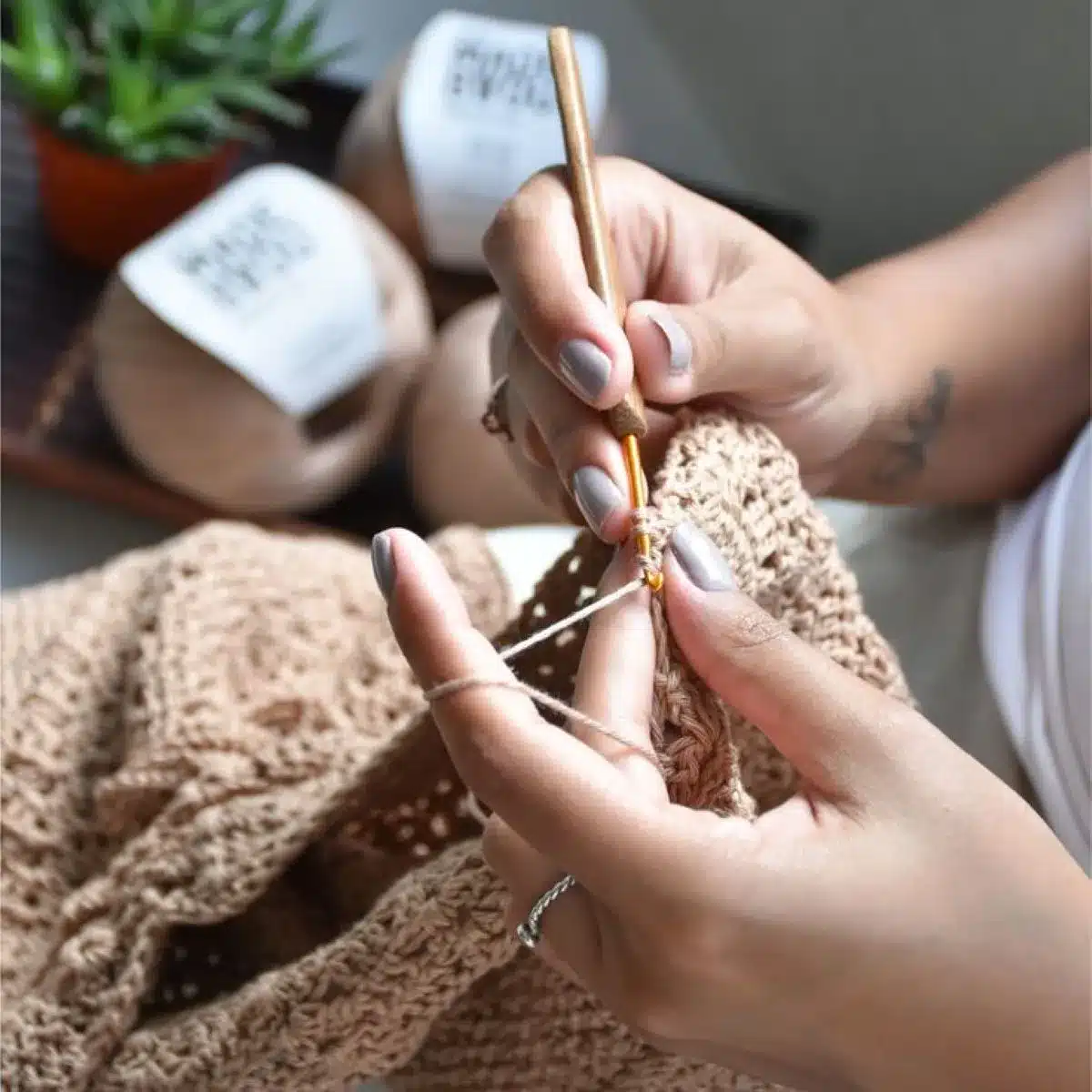 Pessoa fazendo crochê com linha bege e agulha, criando uma peça artesanal.