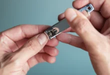 Mãos segurando um cortador de unhas em fundo neutro.