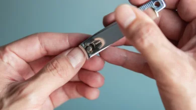 Mãos segurando um cortador de unhas em fundo neutro.