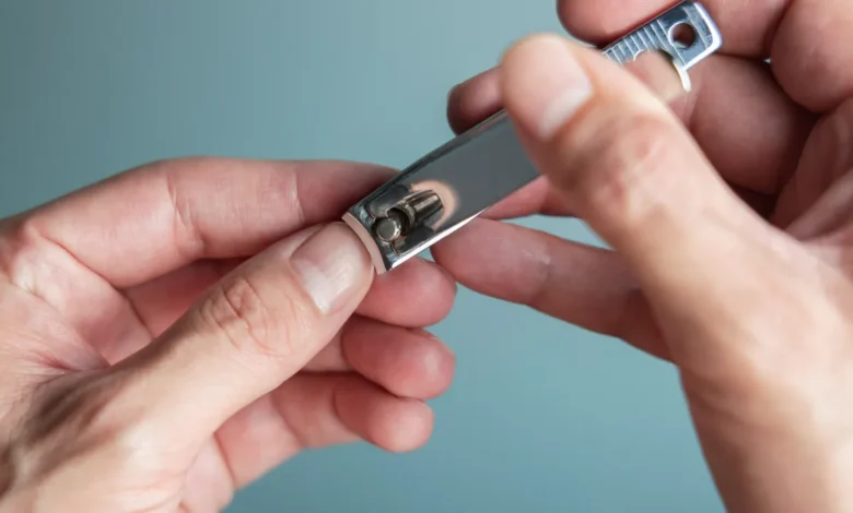 Mãos segurando um cortador de unhas em fundo neutro.
