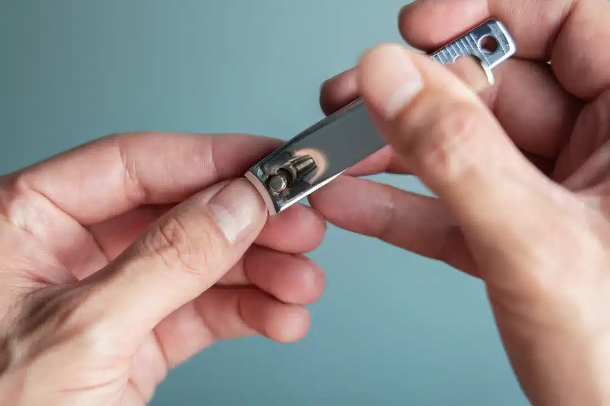 Mãos segurando um cortador de unhas em fundo neutro.