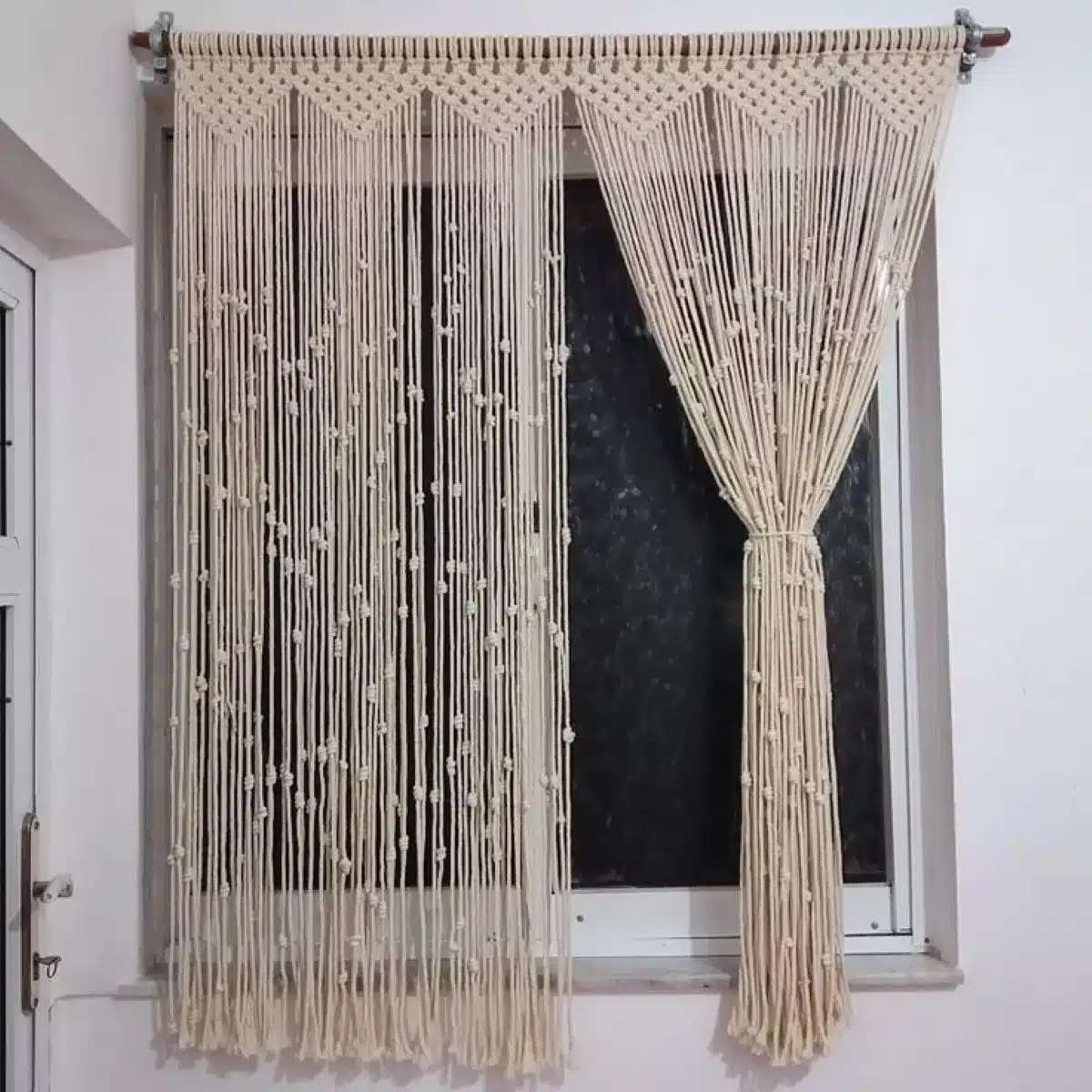 Cortina de crochê feita à mão com fios naturais e detalhes delicados, pendurada em uma janela.