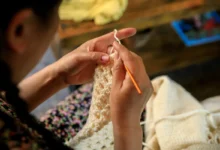 Mãos femininas confeccionando peça de crochê com agulha laranja.