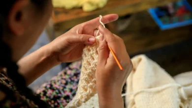 Mãos femininas confeccionando peça de crochê com agulha laranja.