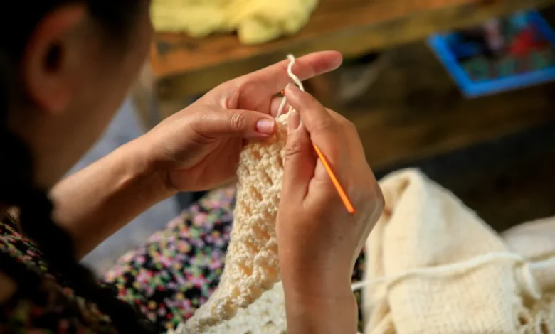 Mãos femininas confeccionando peça de crochê com agulha laranja.