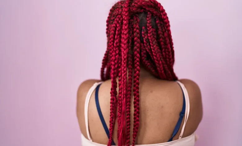 Mulher de costas com tranças box braids vermelhas, estilo crochĂȘ em destaque.