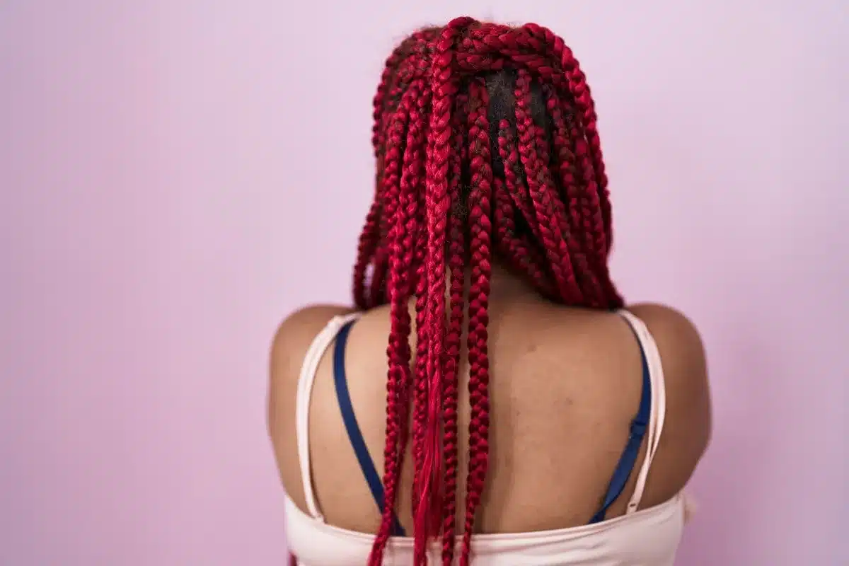Mulher de costas com tranças box braids vermelhas, estilo crochê em destaque.