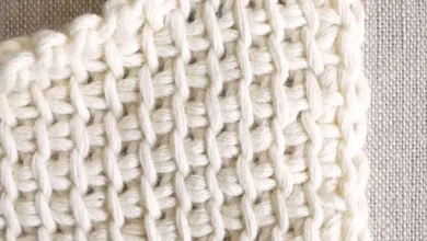 Close-up de crochê com pontos bem definidos e agulha vermelha no fio branco.