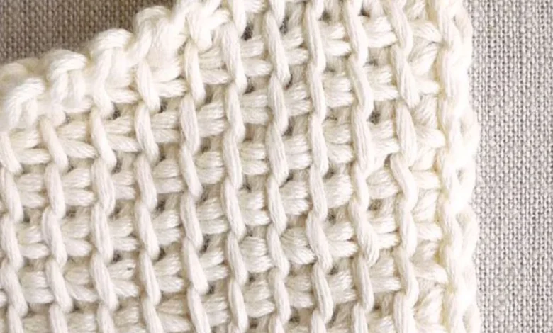 Close-up de crochĂȘ com pontos bem definidos e agulha vermelha no fio branco.