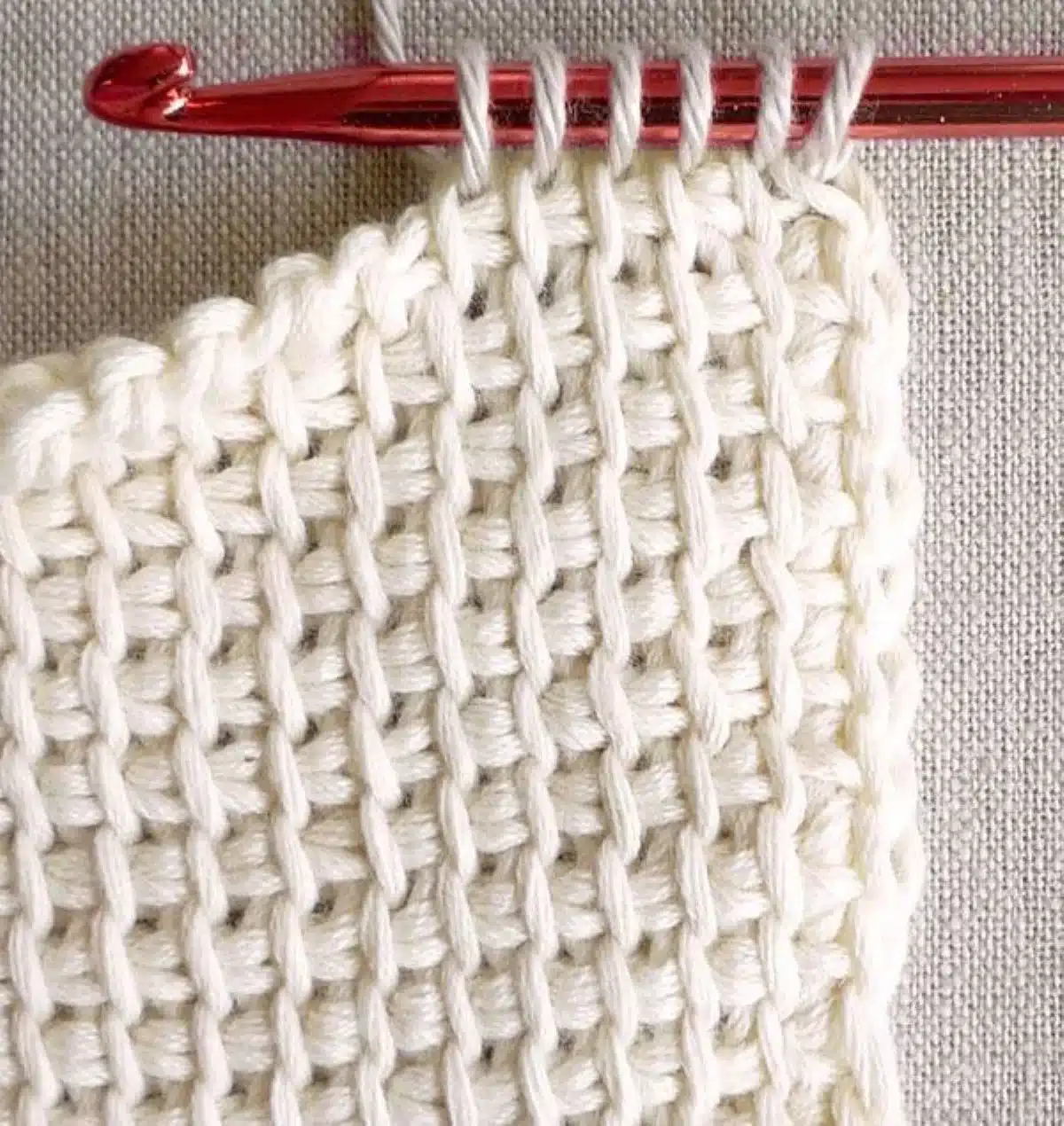 Close-up de crochê com pontos bem definidos e agulha vermelha no fio branco.