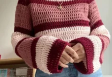 Blusa de crochê com listras em tons de rosa e vermelho, com mangas longas e detalhes de acabamento listrado.