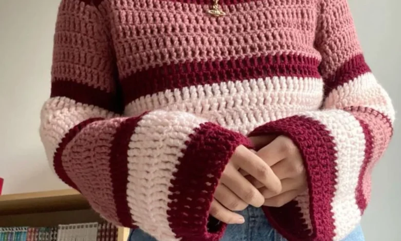 Blusa de crochê com listras em tons de rosa e vermelho, com mangas longas e detalhes de acabamento listrado.