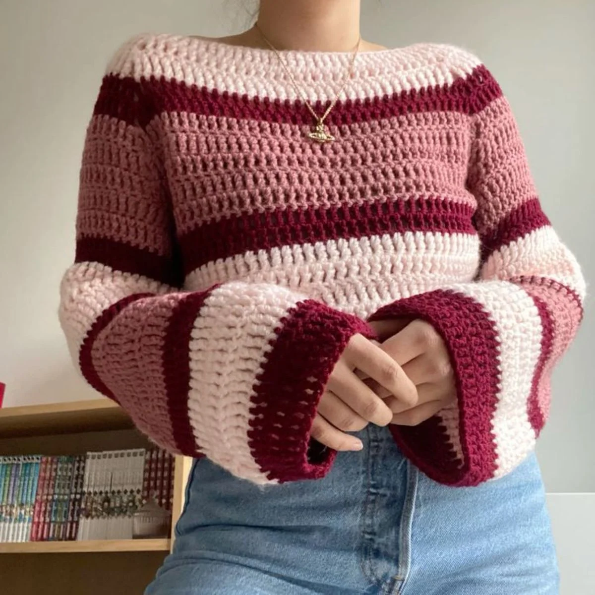 Blusa de crochê com listras em tons de rosa e vermelho, com mangas longas e detalhes de acabamento listrado.