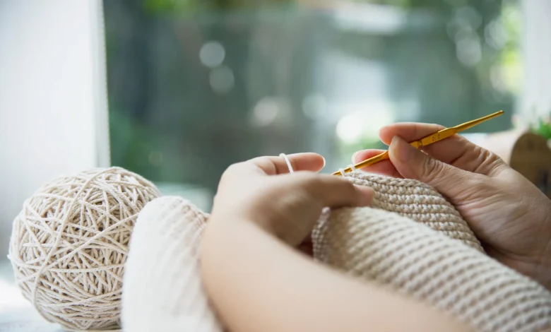 Mãos trabalhando com crochê, criando peças aconchegantes para o inverno de 2025.