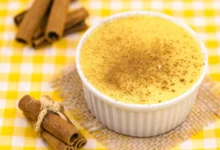 Curau de milho com pó de canela polvilhado sobre ele em fundo de mesa xadrez