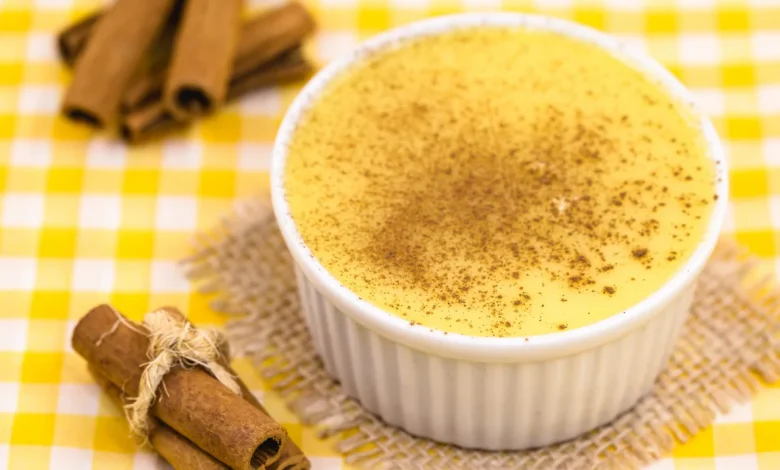 Curau de milho com pó de canela polvilhado sobre ele em fundo de mesa xadrez