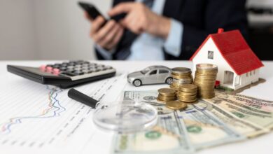 Elementos representando finanças, como moedas, casa em miniatura, carro e calculadora