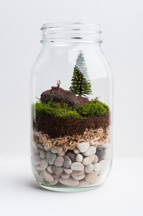 Terrário decorativo montado dentro de pote de vidro com pedras, musgo e miniaturas.