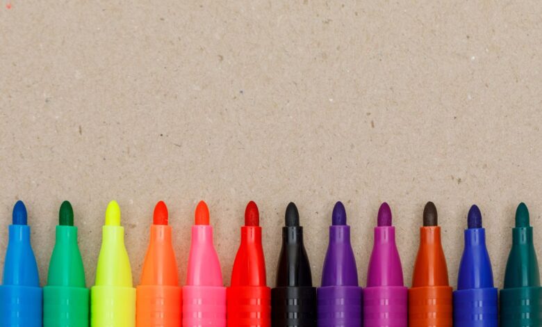 Canetinhas coloridas enfileiradas sobre uma superfície de papel, usadas para colorir livros como os da Bobbie Goods.