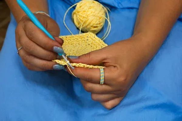 Pessoa praticando crochê com fio amarelo e agulha azul.
