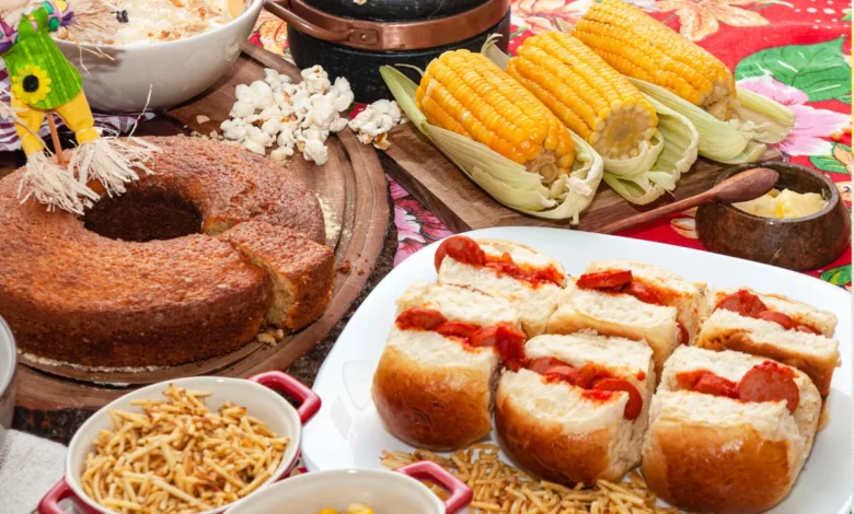 Mesa com comidas típicas de festa junina, incluindo bolo, milho, cachorro-quente, pipoca e amendoim, com decoração festiva.