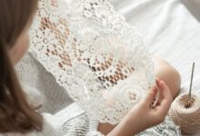 Mulher segurando peça delicada de crochê feita à mão com linha clara e agulha