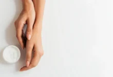 Mãos femininas bem cuidadas com creme hidratante, representando rotina de cuidado com unhas e pele.